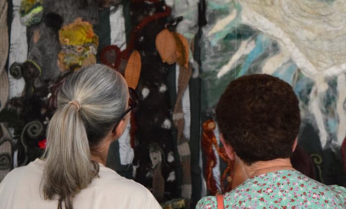 Two women admiring artwork in the gallery. The picture is of the back of their head.